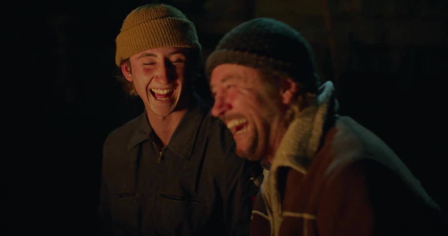Men sit laughing and talking lit by light from fire