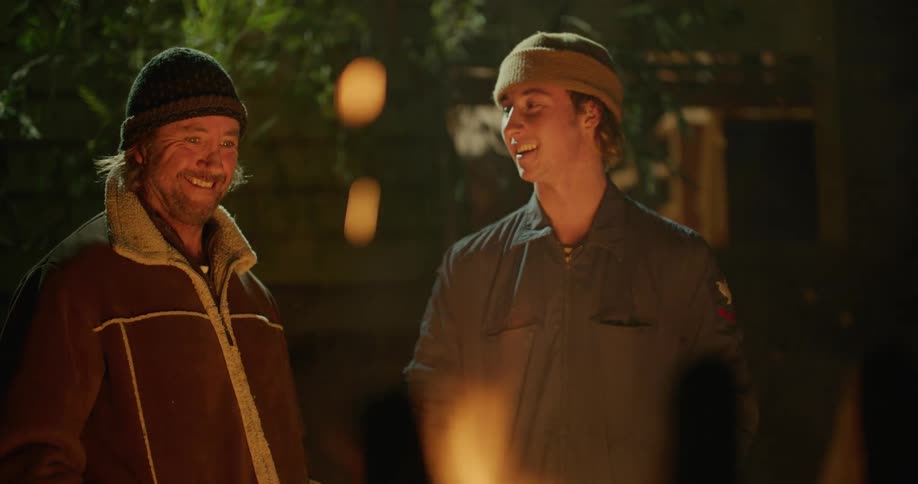 Two men smiling while talking next to a bonfire at night