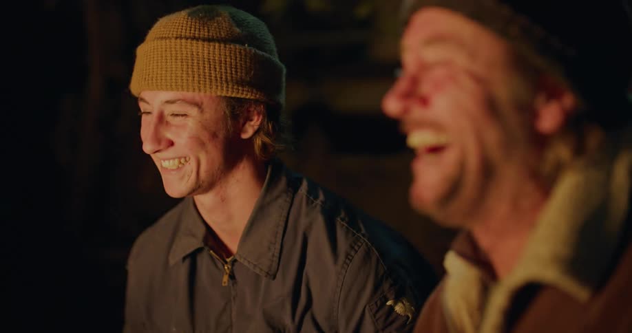 Father and son talking and laughing while sitting in front of a campfire at night