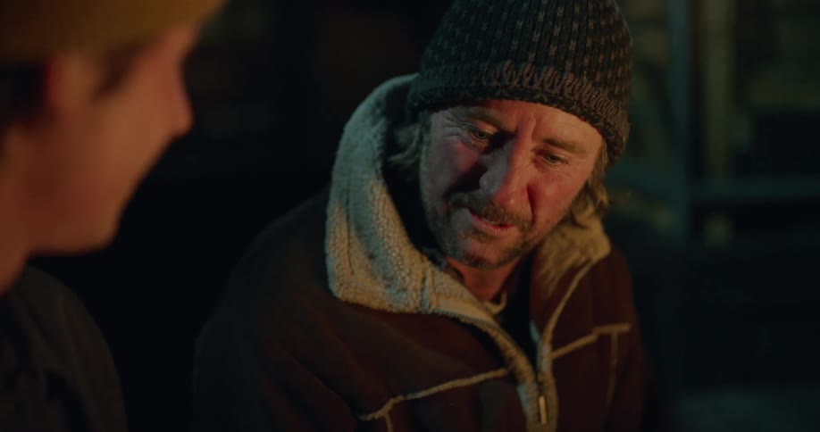 Two men talking and sharing while sitting in front of a campfire at night