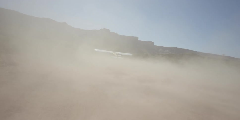 A small yellow single engine plane landing on a dirt runway in the desert