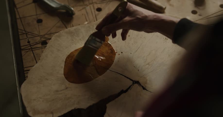 Stain is poured on a tree trunk and then a woman uses a brush to rub it in
