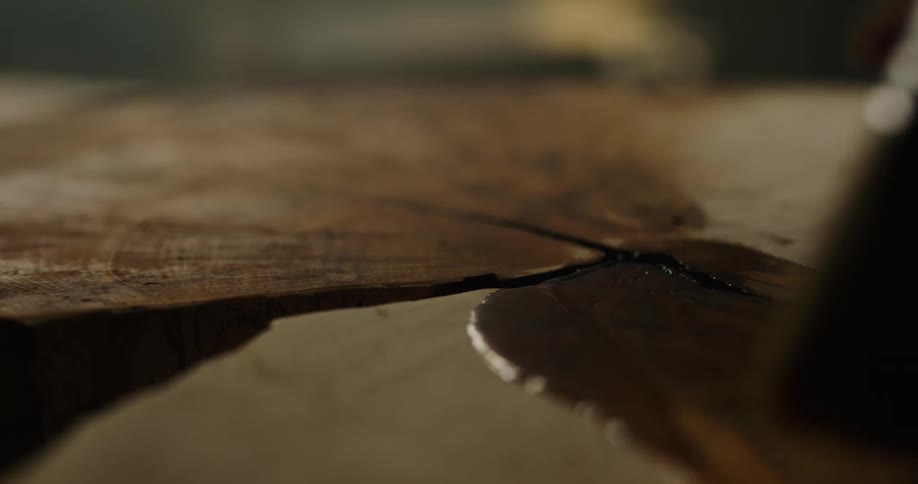 Stain being poured on a tree trunk and brushed on