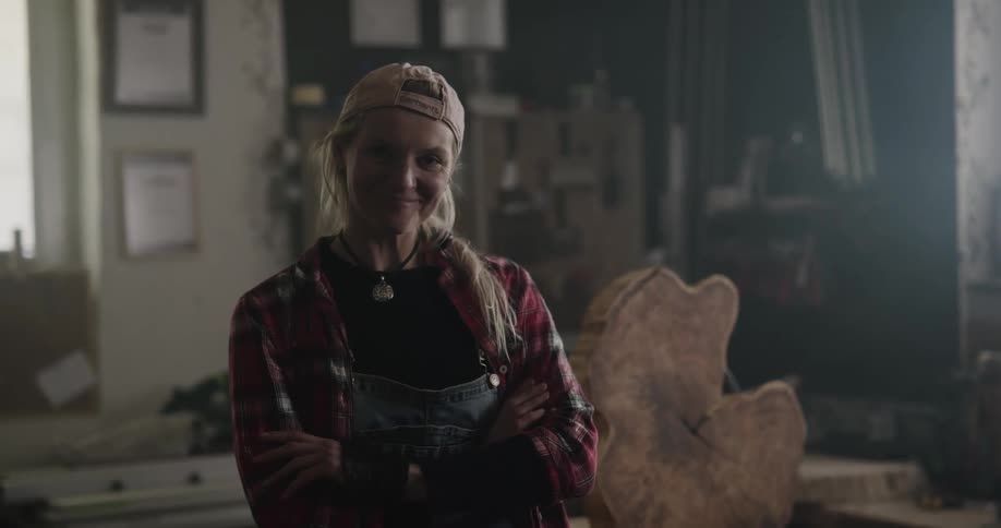 A carpenter smiles into the camera while standing in a workshop during the day