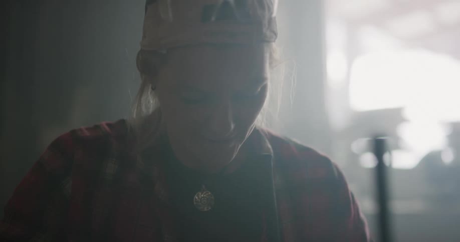 A woman with a hat using an electric drill and a screw on a table