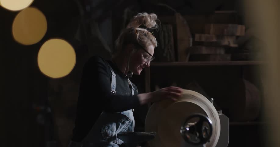 Woman turning a wooden bowl on a lathe inside a dimly lit workshop