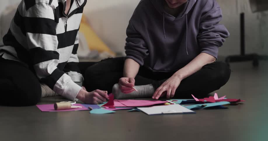 A woman and a teenage boy sitting on the floor of a room handcrafting with colored paper