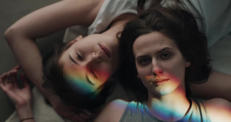A rainbow light shining on a lesbian couple lying next to each other