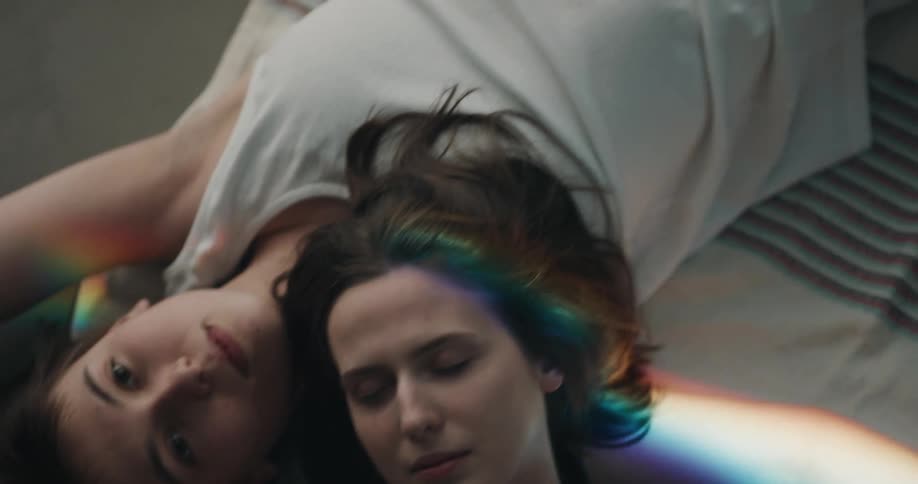 Rainbow light passes over a lesbian couple laying on the floor wearing underwear