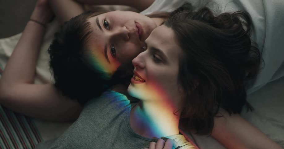 Two people lying down heads together but feet opposite of each other have prism rainbow lights across their heads