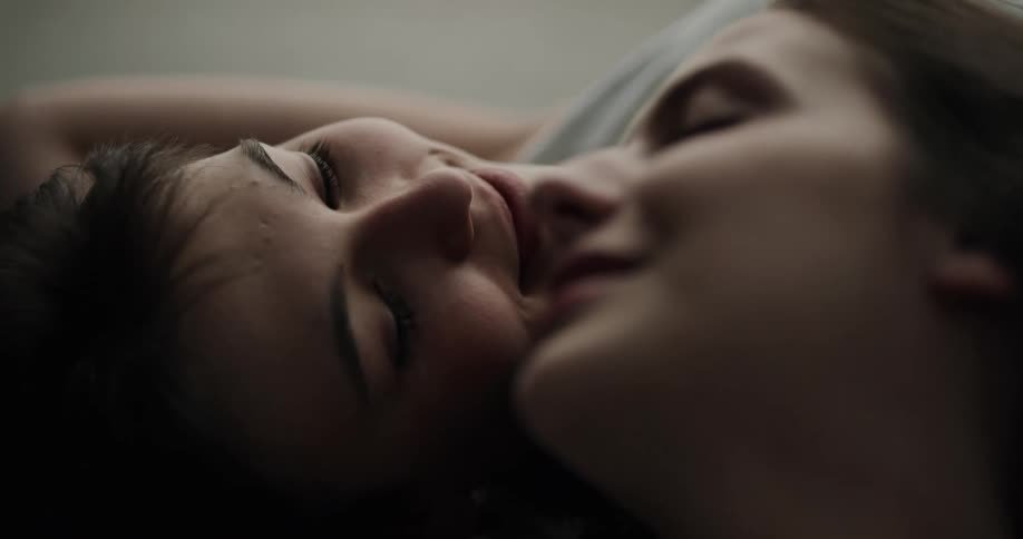 Two teenage girls lie with their heads side by side as they cuddle and talk
