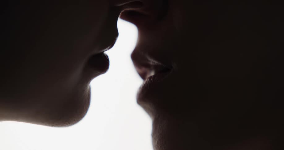 Two in profile people kiss cast into shadow by light