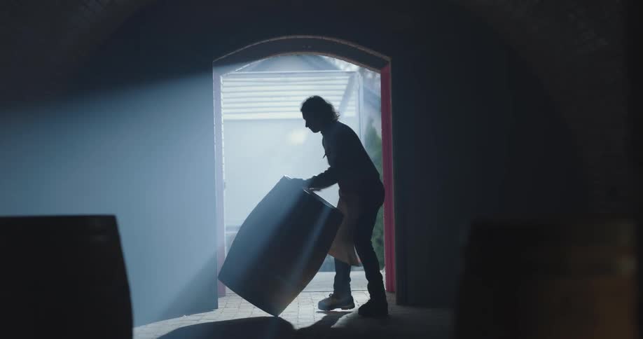Man wearing apron rolls barrel into dark room