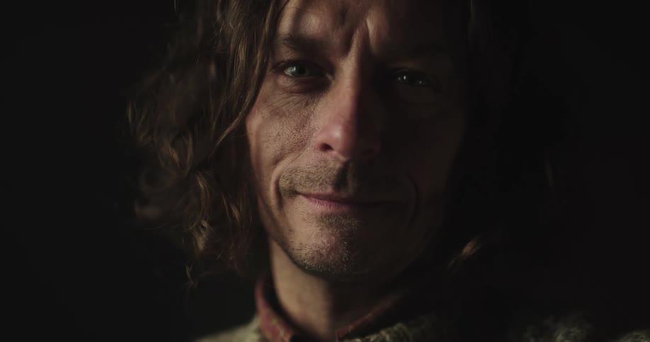 Long haired man turns to look at the camera inside a dark room