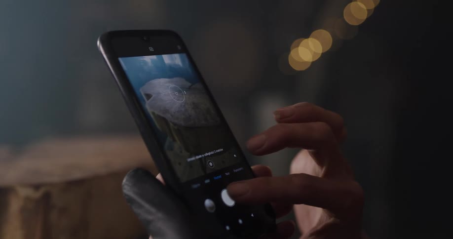 Blonde female carpenter with a cap and a shirt takes pictures of carved log