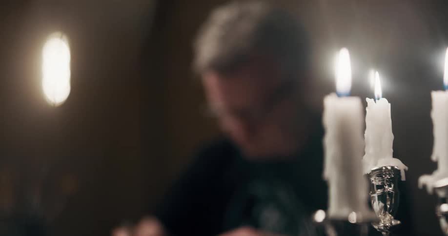 A man sitting in front of a burning candle at a desk working stops to look up and smile at the camera