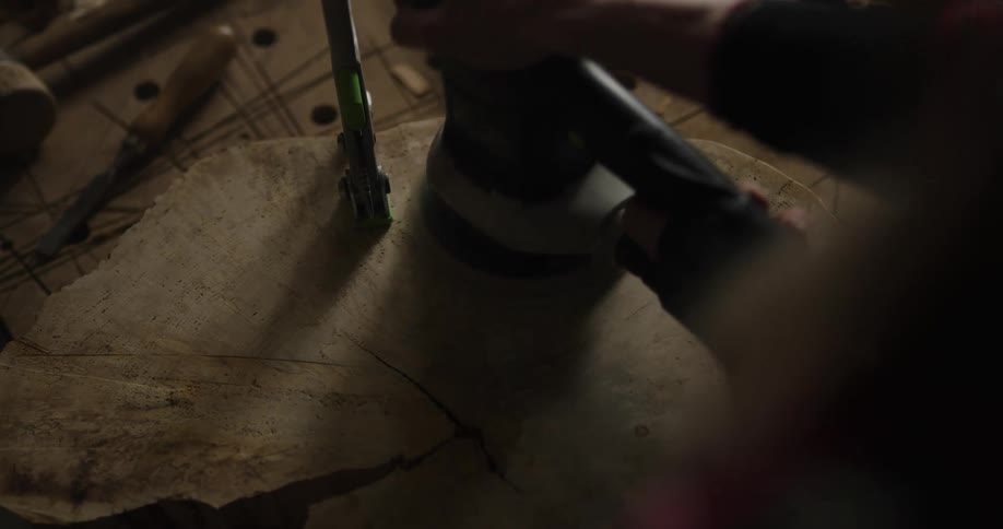 Person smooths sliced piece of tree with power tool