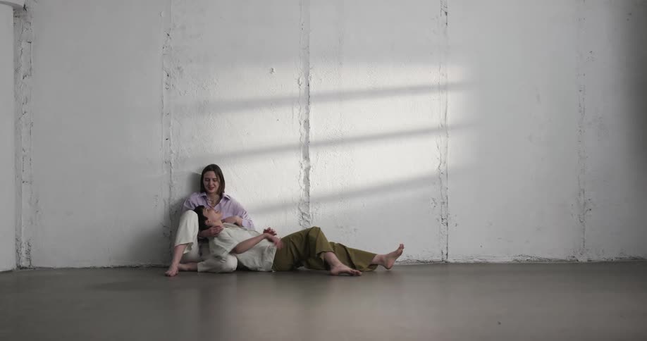 A teenage girl pulls another girl down to lie her head in her lap and she strokes her hair
