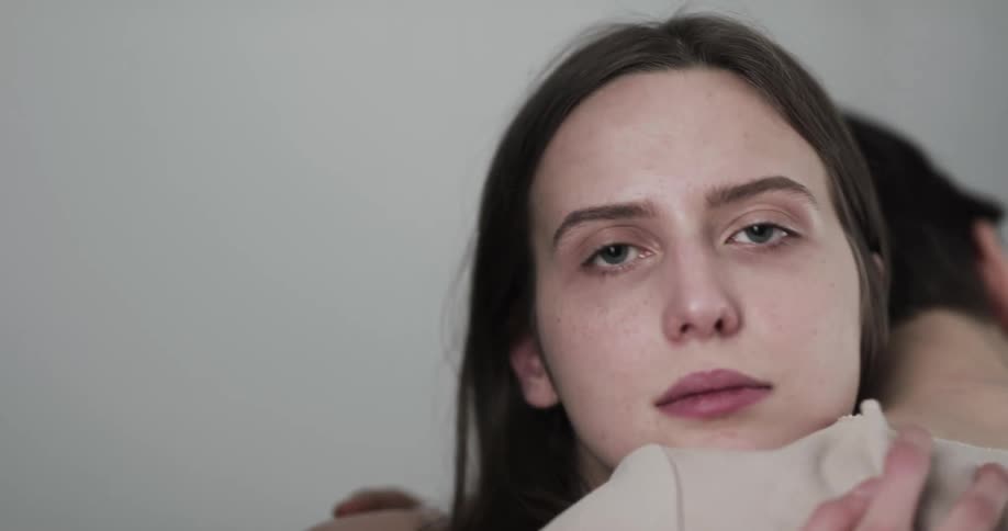 A young woman kisses another woman and gazes into the camera as they embrace