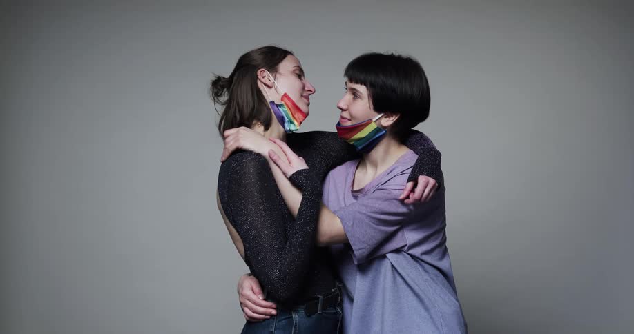 A pair of woman affectionately embrace each other and smile while posing in a studio