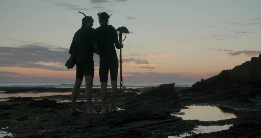 Two silhouetted men standing on a beach at sunset while spear fishing