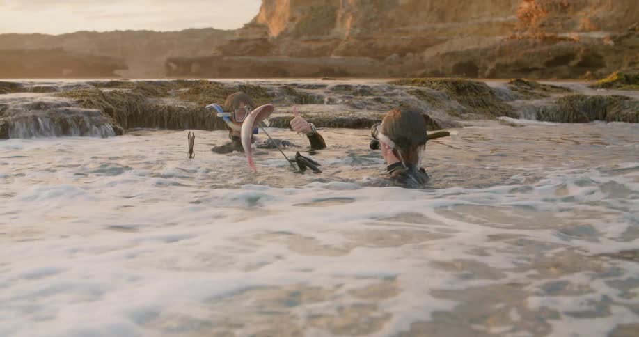 Two men with scuba gear in the ocean with land the sky and clouds in the background