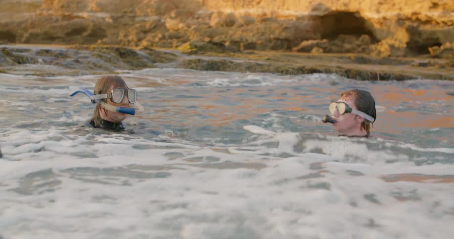 Two men snorkeling among foaming waves gesture to communicate