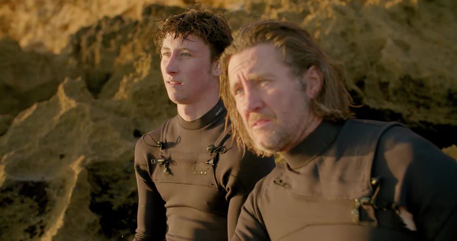 Two men wearing water suits gesture and talk looking out