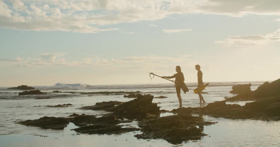 Two men walk on the shore with fishing gear and point in to the distance