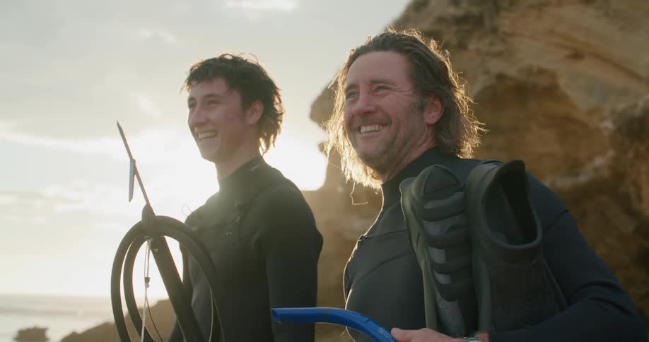 Two men are standing outdoors by the coast at dusk
