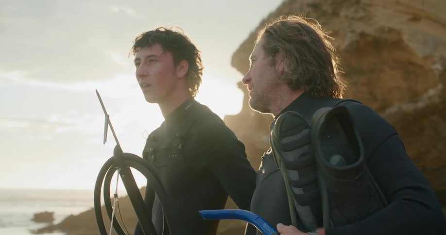 A father and son talk as they stand on the shore holding fishing gear