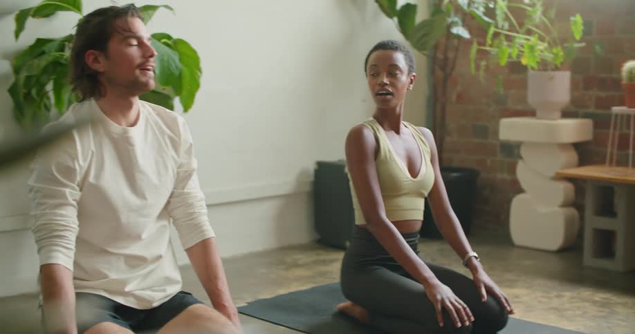 A woman and woman smile at each other after sitting back up from a forward stretching yoga pose