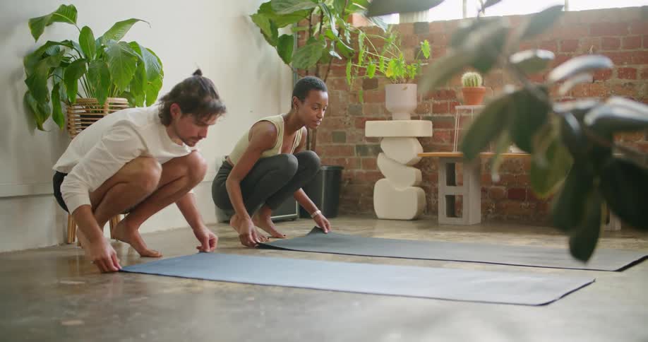 A man and a woman unrolling a mat on the floor with a wall and window in the background