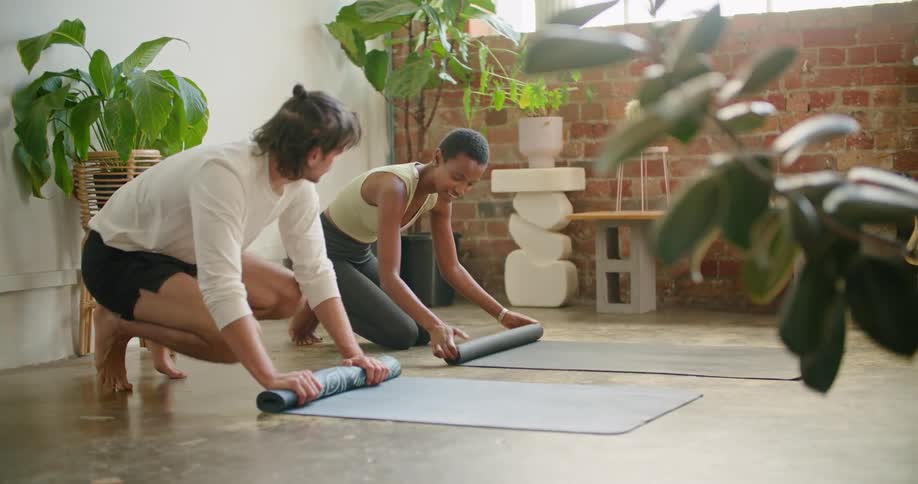 A man and woman roll up yoga mats from the floor