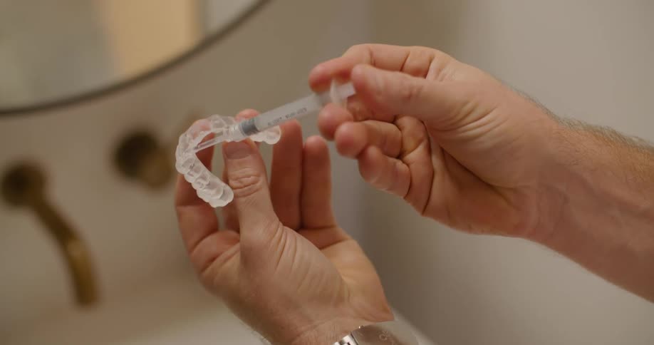 A person in a bathroom applying gel to a teeth whitening strip