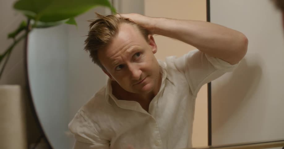 A man checks his hairline in the mirror