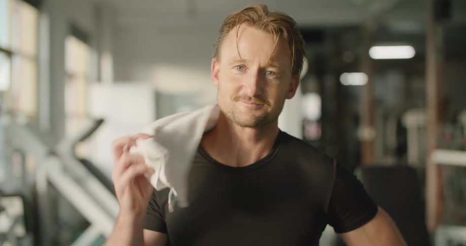 A man who just completed a workout wipes sweat from his face while posing for the camera