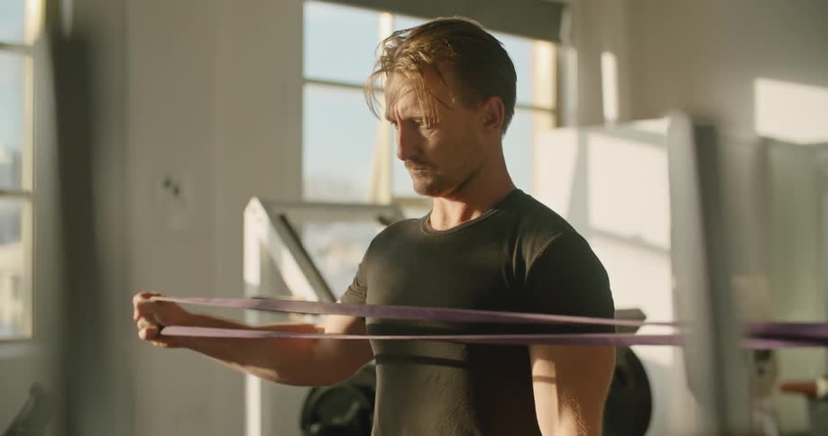 A man slowly and steadily performs and exercise using a long elastic strap
