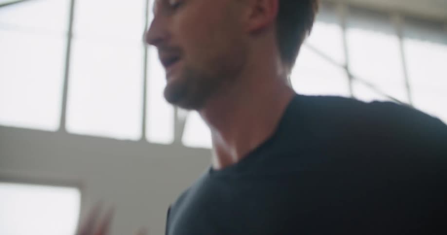 A man in a gym running on a treadmill with equipment and windows in the background