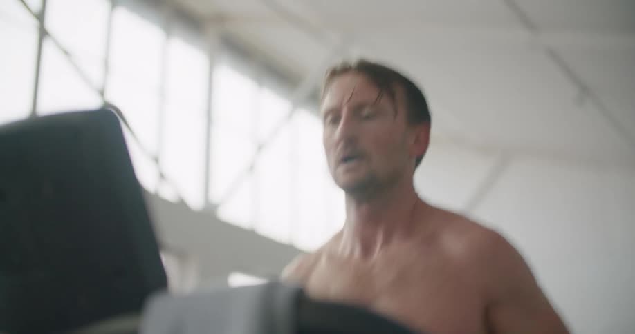 A man in a gym running on a treadmill with equipment and windows in the background