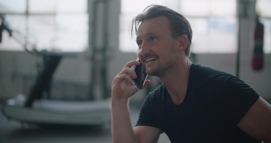 Man sitting on a chair in the middel of a gym talking on the phone
