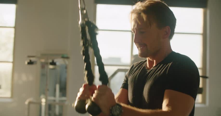A man exercises using a weights attached to a pulley in a fitness room