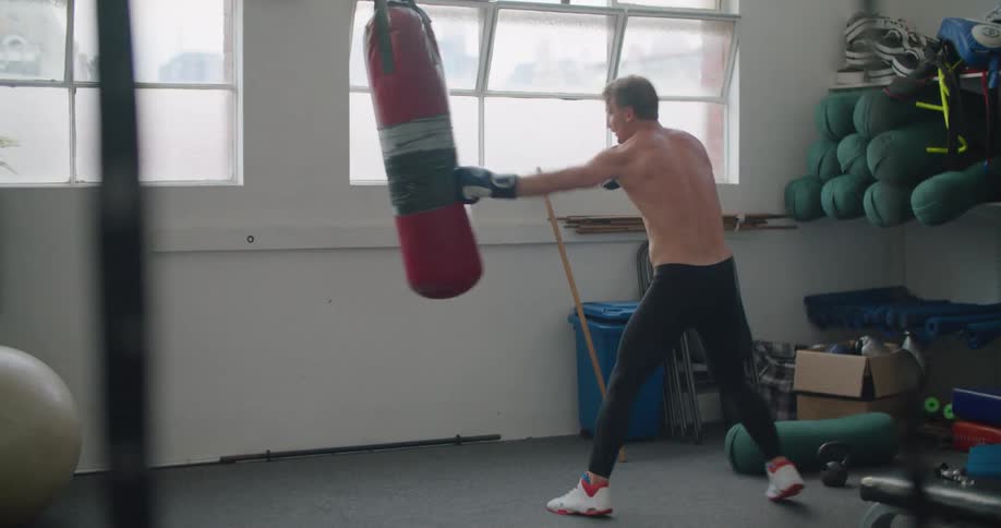 Shirtless man wearing boxing gloves sparring with a punching bag