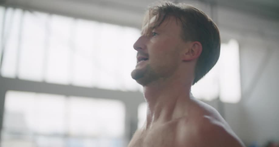 A shirtless man lifts weights in a gym during the day