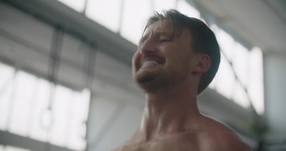 A man lifts weights in a gym while shirtless