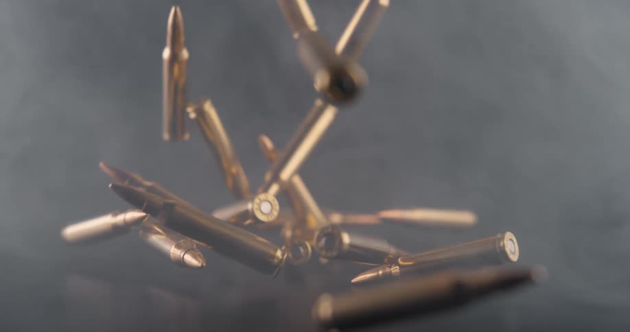 A cascade of brass rifle shells fall down and bounce upon a black surface as smoke swirls through the air