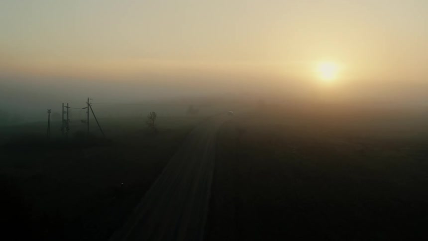 A vehicle driving on a road with the sun the sky and clouds in the background