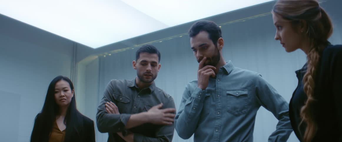 A group of coworkers hold a discussion while standing around a table indoors