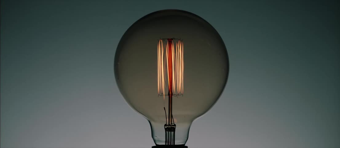 Light bulb filament glows and dims behind gray tinted glass