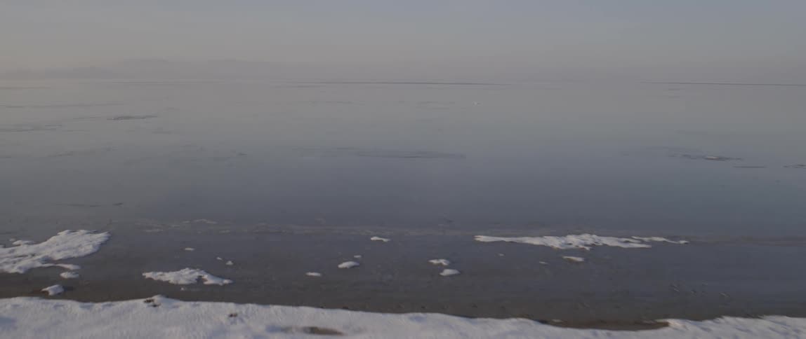 Close up of some calm water leading to snow covered shore